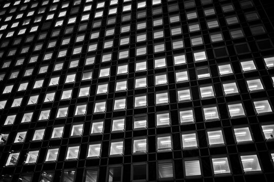 Dark building facade with illuminated windows forming a geometric grid in Paris photographed at night with repeating windows filling the dark facade