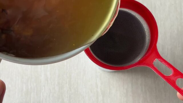 A traditional herbal decoction&mdash;strained to create a healthful beverage from a blend of spices such as red ginger, galangal, turmeric, and lemongrass&mdash;being poured into a blue glass.