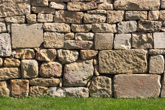 Rough old stone wall texture with green grass foreground