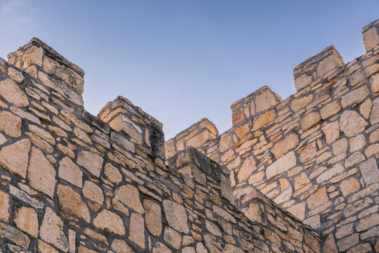 Low angle view of medieval stone fortress wall battlements against clear blue sky
