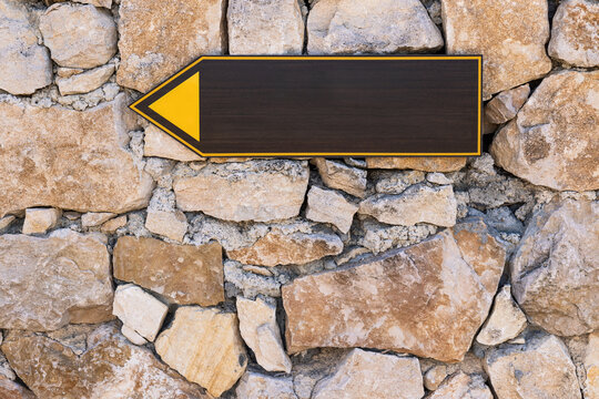 Blank wooden directional arrow sign mounted on rustic stone wall