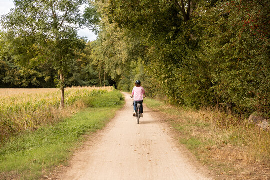 Femme &agrave; v&eacute;lo sur un chemin en lisi&egrave;re de for&ecirc;t bord&eacute; d'arbres verts et de champs