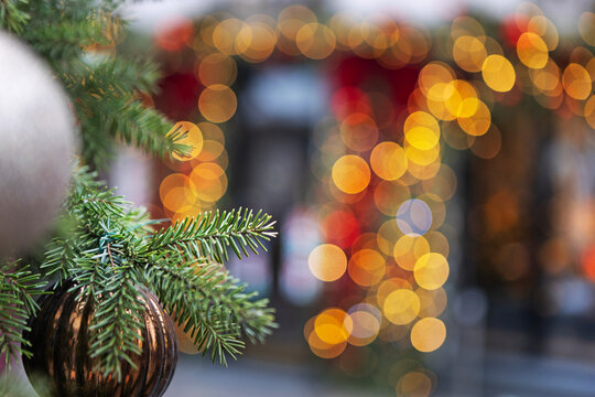 Dark bronze Christmas tree toy balloon is hanging on green fir branch. Warm golden highlights of side fade behind. Background for New Year's or Christmas greetings. Copy space