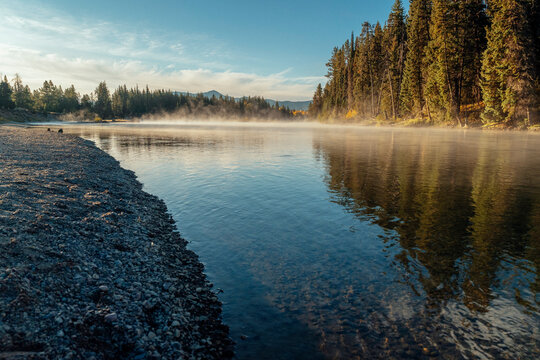 Exposed gravel shoreline borders a calm river beneath morning mist.