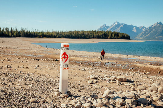 Person walks across a broad exposed lakebed toward receded water.