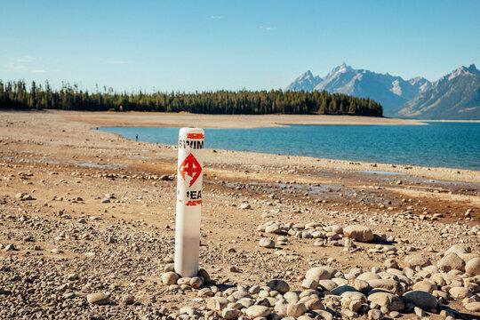 Marker post rises from a dry rocky lakebed beside receded water.