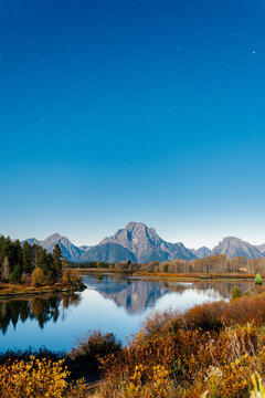 Mountain range reflected on river during full moon with star trails.