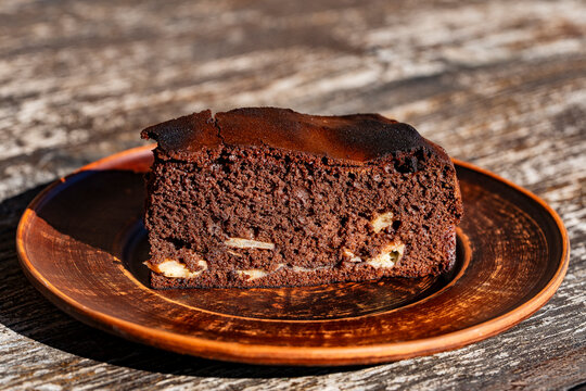 Slice of homemade chocolate cake on clay plate. Closeup of delicious piece of chocolate sponge cake or brownie with filling served on rustic ceramic plate over wooden table