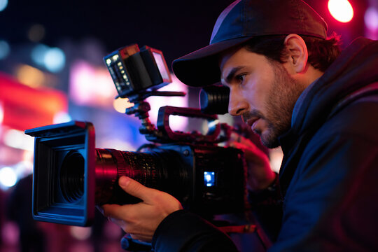 A man operating a professional video camera in a dimly lit, urban or event setting.