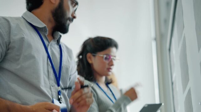 Engineer writing technical information on a glass board while collaborating with a colleague in a modern technology office.

