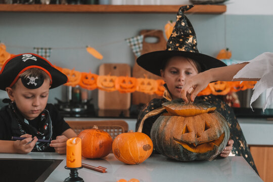 A medium shot of children in Halloween costumes decorating their home, carving a pumpkin, and eating gummy candies. They are playing together and celebrating Halloween in the kitchen. Trick or treat.