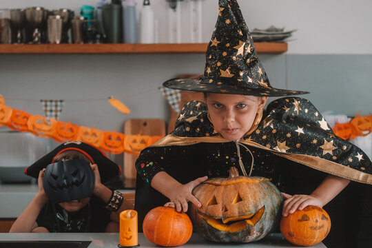 A medium shot of children in Halloween costumes decorating their home, carving a pumpkin, and eating gummy candies. They are playing together and celebrating Halloween in the kitchen. Trick or treat.