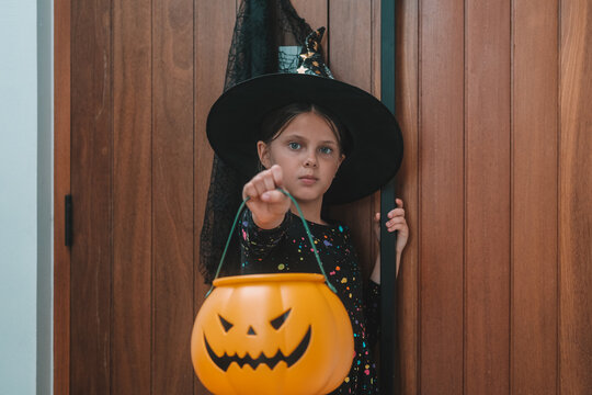 A portrait of a girl in a witch costume, out trick or treating with a pumpkin shaped basket. Trick or treat. An autumn children's celebration during the spooky season.