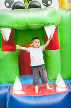 A delighted child stands barefoot in a colorful dragon-themed bounce house, stretching his arms in pure excitement. The setting is bright, filled with cheer as kids enjoy their time.