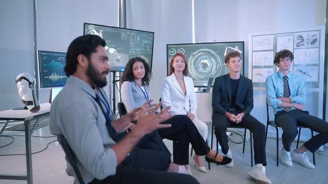 Diverse engineering team attending a robotics technology presentation in a modern laboratory with digital displays, technical drawings and robotic equipment.
