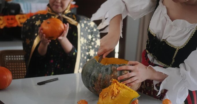 A close-up shot of the hands of children and their mother carving Halloween pumpkins on the kitchen table. Preparing and decorating the home for the main autumn holiday for children. Trick or treat.