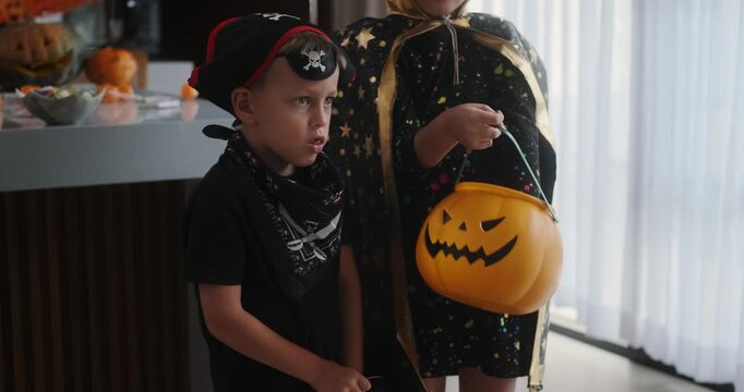 Medium shot of children in Halloween costumes looking for treats in pumpkin-shaped baskets. Trick or treat. Celebrating Halloween with children and collecting candy.