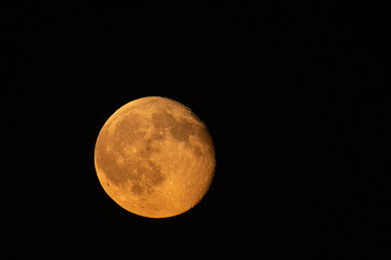 Dramatic close-up of a waning autumn moon glowing with an intense orange and red hue against a pitch-black night sky © CesareFerrari