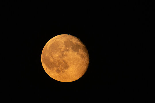 Dramatic close-up of a waning autumn moon glowing with an intense orange and red hue against a pitch-black night sky