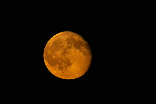 Dramatic close-up of a waning autumn moon glowing with an intense orange and red hue against a pitch-black night sky