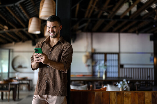 Happy male digital nomad checking smartphone while enjoying vacation at tropical resort