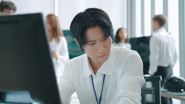 Engineer reviewing technical documents and project information at a computer workstation while colleagues collaborate in the background.
