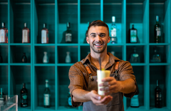 Young smiling handsome man waiter serving fruit juice, smoothie while working in a cafe.