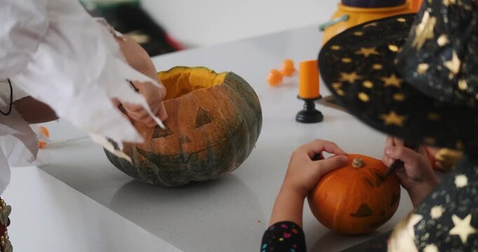 A close-up shot of the hands of children and their mother carving Halloween pumpkins on the kitchen table. Preparing and decorating the home for the main autumn holiday for children. Trick or treat.