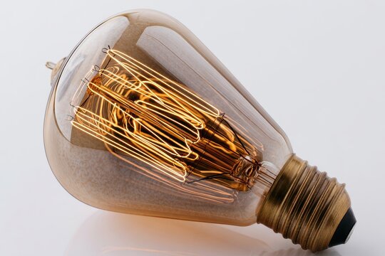 Close up of a vintage edison light bulb with intricate glowing filament isolated on white background