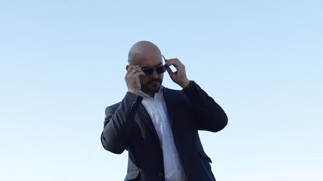 Successful bald businessman putting on sunglasses outdoors