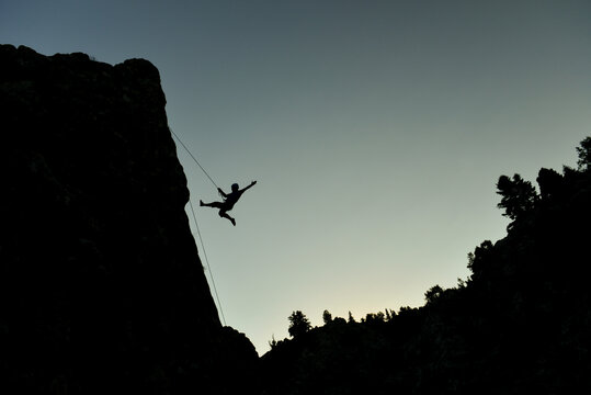 Silhouette of a rock climber hanging on a rope at sunset celebrating success