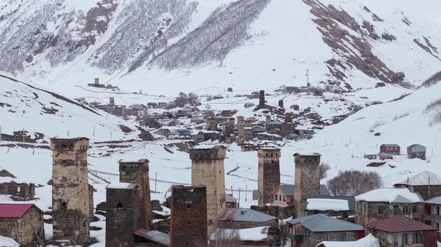Telephoto footage showcasing the layered architecture of Ushguli, with snow-covered homes in the foreground and the neighboring settlement framed against the winter landscape of the Caucasus Mountains