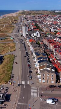 Vertical aerial drone clip of coastal boulevard, North Sea beach, sand dunes, and seaside town architecture in Katwijk aan Zee, South Holland, Netherlands on sunny summer day