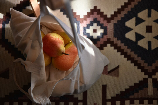 Fresh pears in a canvas tote bag hanging over the traditional kilim pattern rug