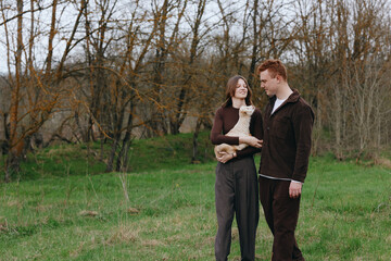 Obraz premium A couple outdoors with a goat kid in a grassy field, smiling at each other. A warm, candid lifestyle moment in a natural setting, perfect for family, animals, and nature themed storytelling.