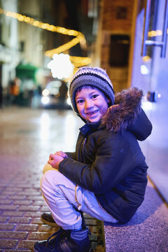 Smiling boy sitting under Christmas lights on city street at night