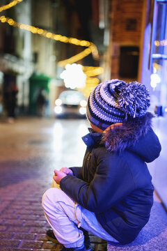 Boy sitting on city street with Christmas lights at night