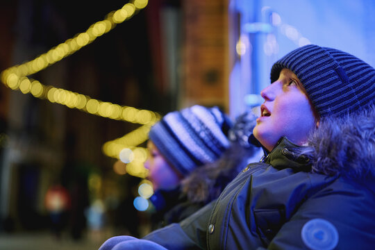 Two boys looking up at festive lights on city street at night
