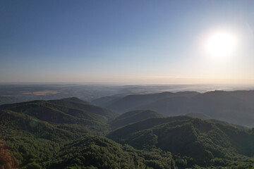 Obraz premium Drone panorama of bright morning sun over vast mountain ranges and hazy green valleys