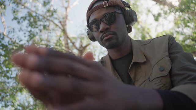 Close up of man wearing sunglasses and ear protection gesturing with his hands in outdoor setting. subject is dressed in military style clothing while interacting expressively