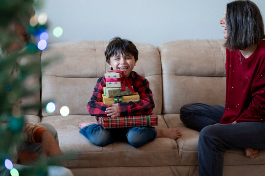 Happy boy holds a stack of gifts on a sofa