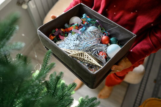 Woman holds a box of Christmas decor indoors to decorate the tree