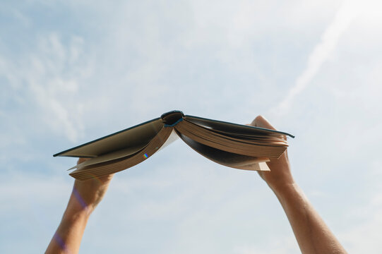 Woman holds an open book up towards the sunny summer sky
