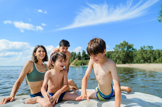 A happy family plays on an inflatable raft in the lake in summer