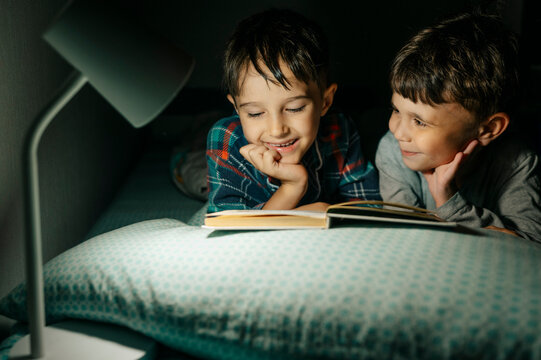 Smiling boy and brother read a book in bed at night