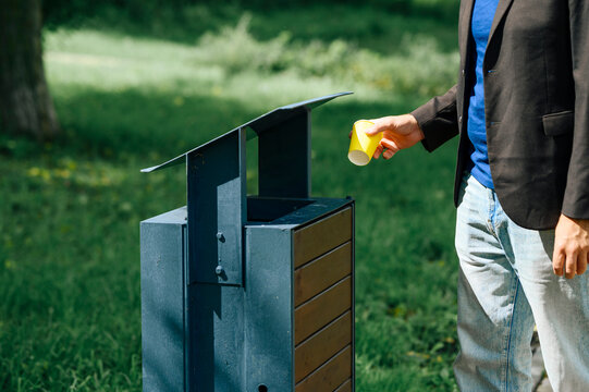 Businessman throws a yellow paper cup into a garbage bin in the park