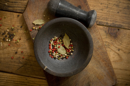 Mortar with dried peppercorns and laurel leaves on wood, elevated view