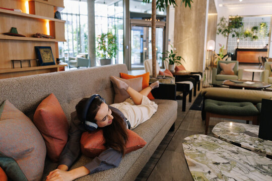 Woman relaxes on a hotel lobby sofa listening to music