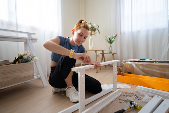 Woman assembles new white furniture on the floor of her apartment