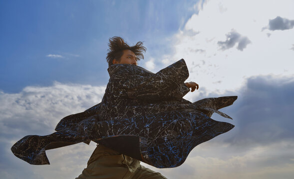 A man performs a dynamic dance in a colorful robe against the sky
